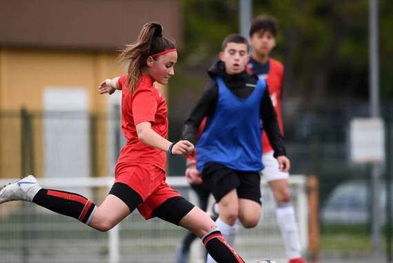 a girl in a red uniform kicking a football ball